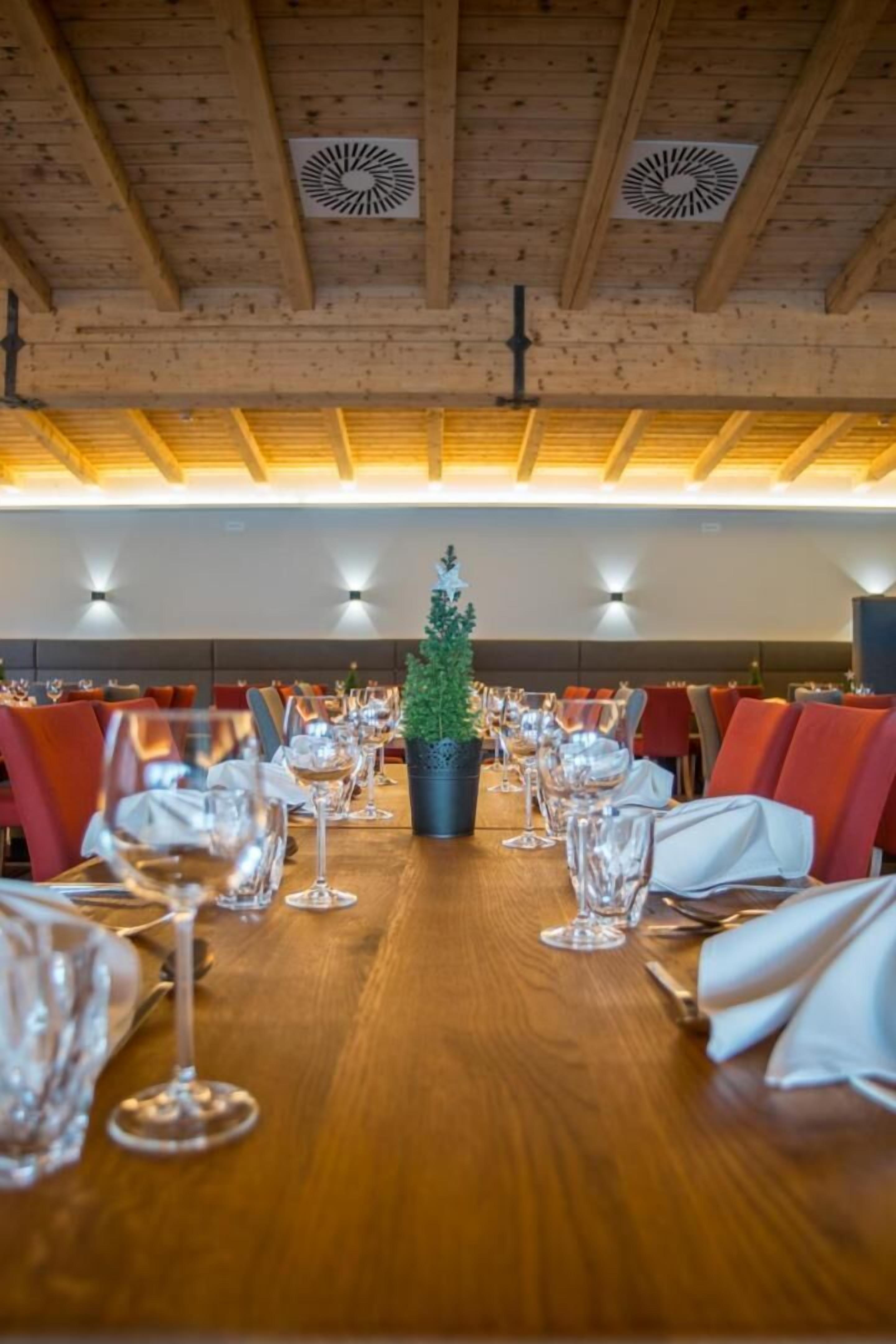 Ein Restaurant mit Holzbalken an der Decke, einer zentral platzierten Pflanze im Topf und roten Sitzmöbeln.
