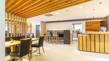 Un interior moderno con vigas de madera en el techo, un área de comedor central con sillas y una mesa, y una cocina con mostrador y electrodomésticos.