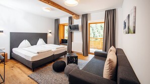 A modern bedroom with a double bed, a sofa, a TV, and a large window with curtains. - Hotel Hirschentenne (Stams)