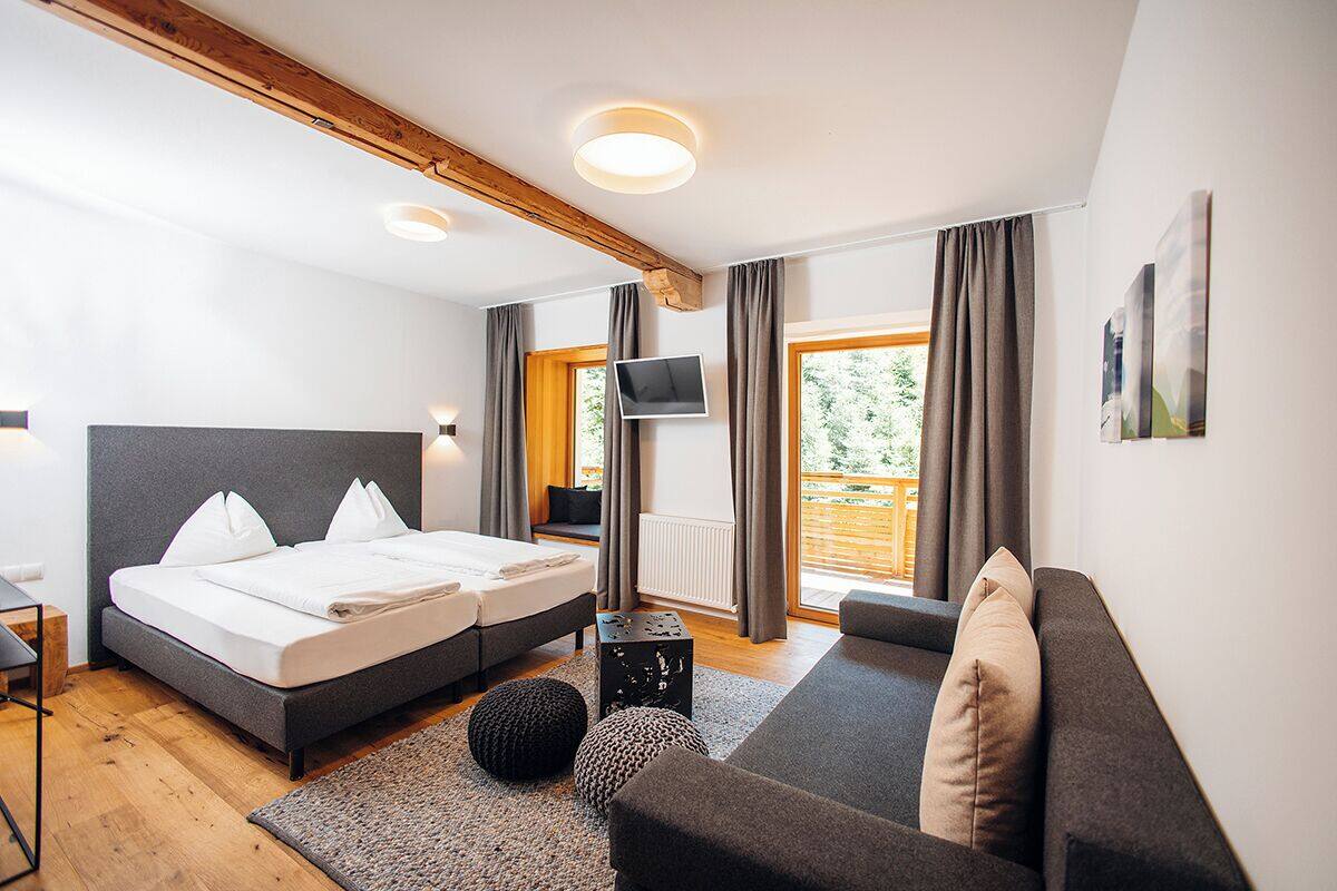 A modern bedroom with a double bed, a sofa, a TV, and a large window with curtains.
