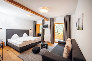 A modern bedroom with a double bed, a sofa, a TV, and a large window with curtains. - Hotel Hirschentenne (Stams)