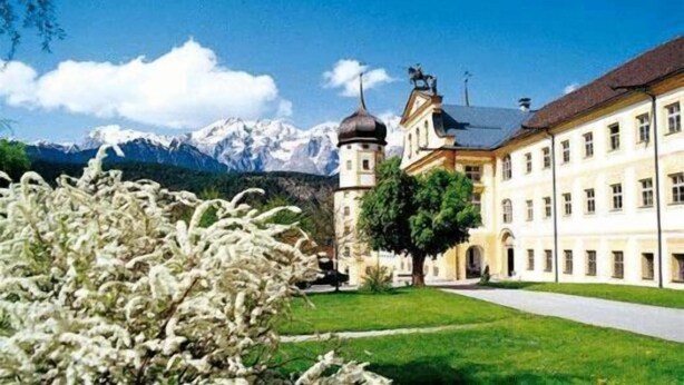A building with a tower, a large lawn, and mountains in the background. - Hotel Hirschentenne (Stams)