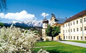 A building with a tower, a large lawn, and mountains in the background. - Hotel Hirschentenne (Stams)