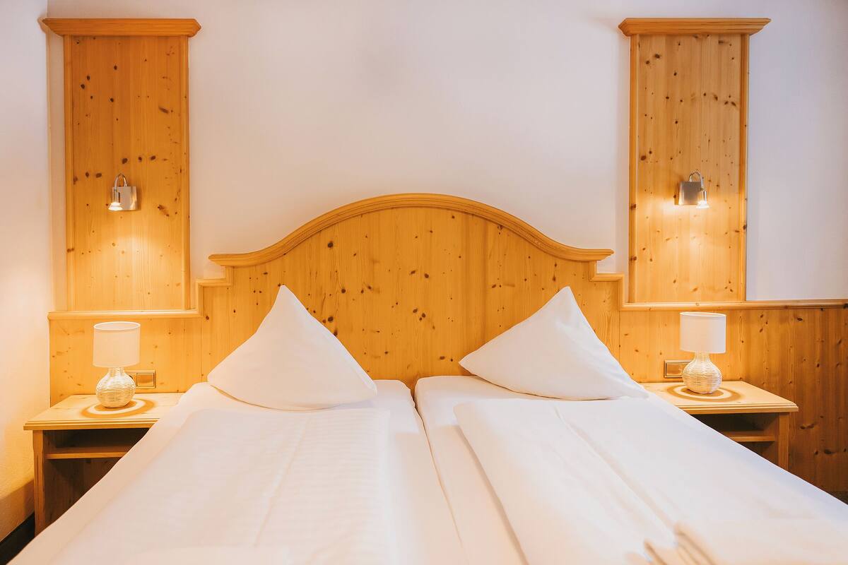 A double bed with a wooden headboard, two bedside lamps, and a nightstand with a lamp.
