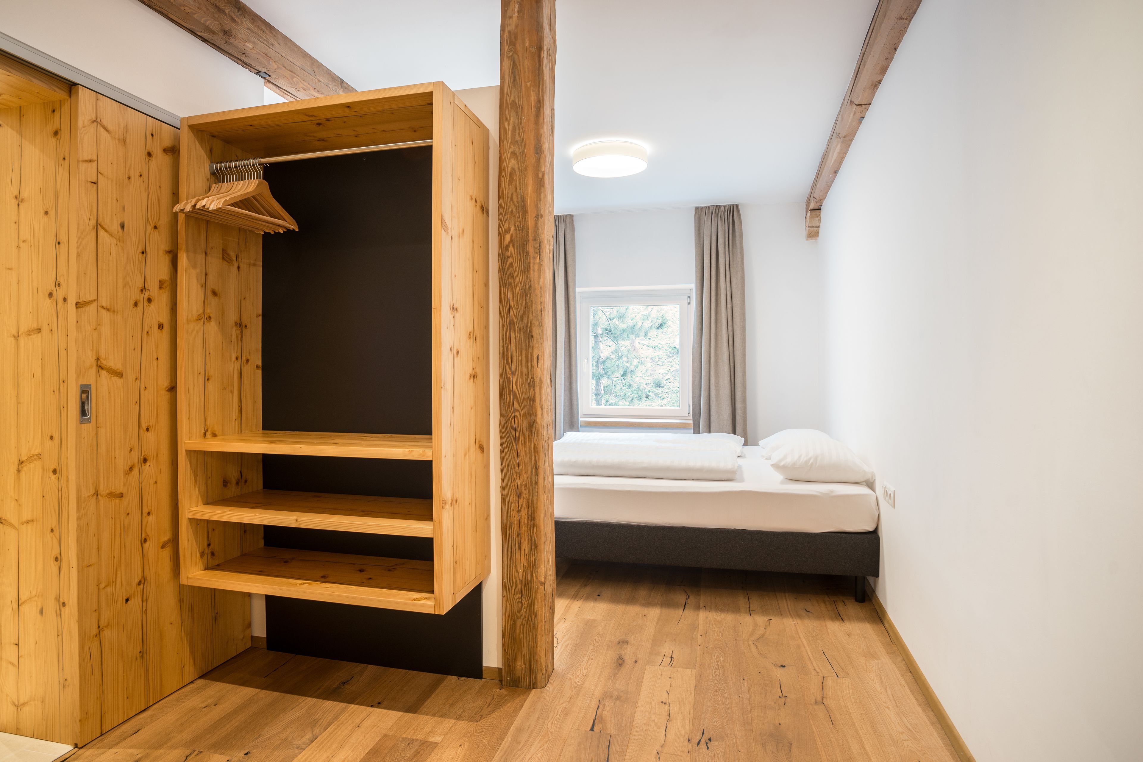 Una habitación con un armario de madera, una cama y un ventanal con cortinas.