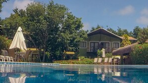 A swimming pool with lounge chairs and umbrellas, surrounded by trees and a building with a thatched roof. - Hotel Recanto da Mata (Tibau do Sul)