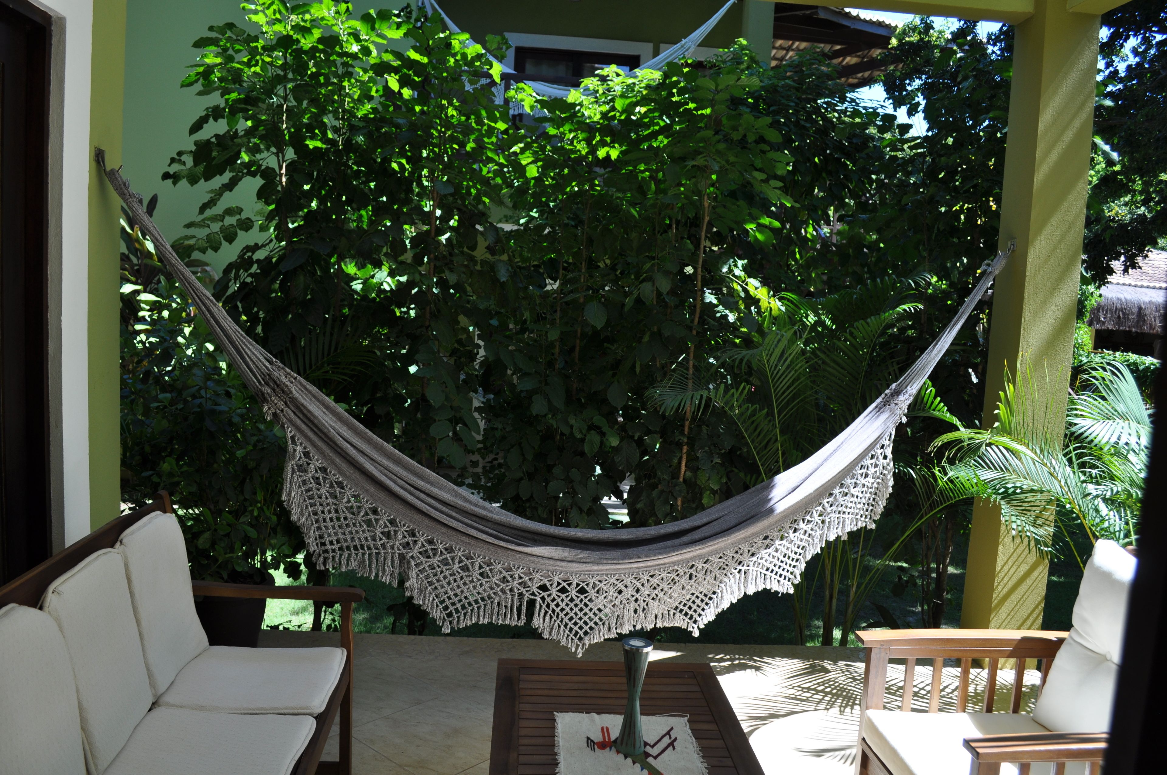 A hammock suspended between wooden posts in a covered outdoor area with chairs and a table.