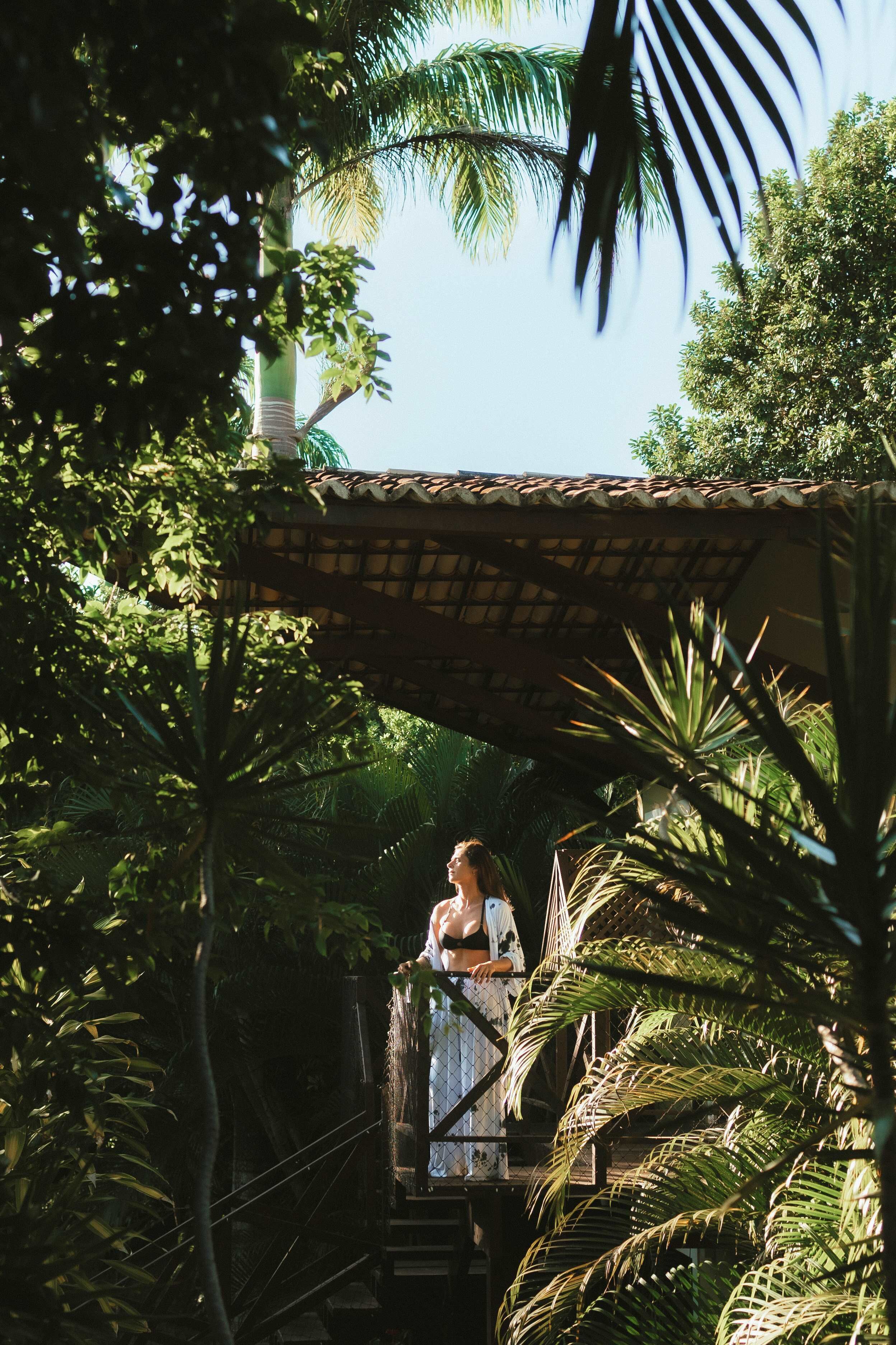 A person on a staircase with a thatched roof, surrounded by lush greenery.