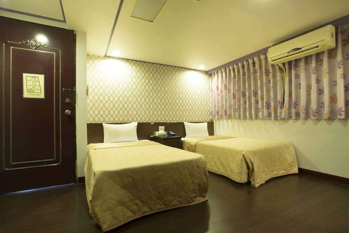 A hotel room with two beds, a wooden door, a patterned wall, and an air conditioning unit.