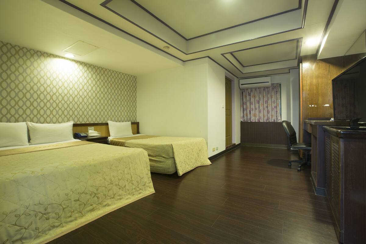A hotel room with two beds, a desk with a chair, and a television.
