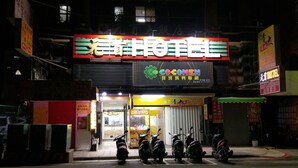 A hotel entrance with a neon sign, scooters parked in front, and various signs in a foreign language. - Chief Hotel (Hsinchu)