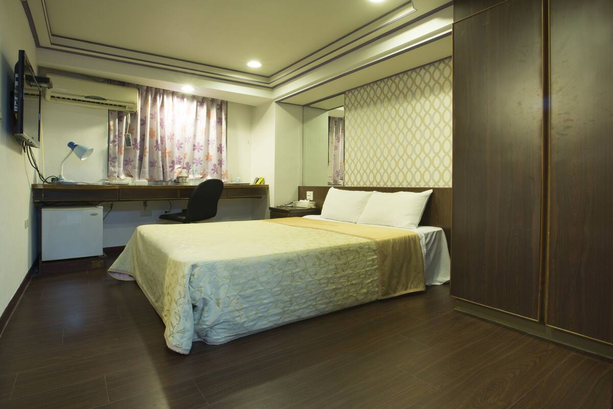 A hotel room with a bed, desk, chair, and wardrobe.