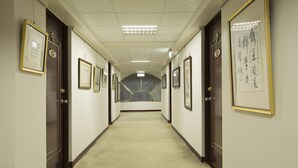 A hallway with framed pictures on the walls, doors on either side, and a carpeted floor. - Chief Hotel (Hsinchu)