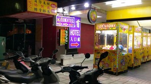 A hotel entrance with a neon sign, a toy story arcade, and several scooters parked outside. - Chief Hotel (Hsinchu)