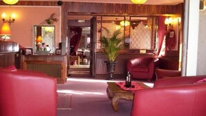 A lobby with red leather sofas, a reception desk, and a potted plant. - Hôtel la Croix Couverte (Mayenne)