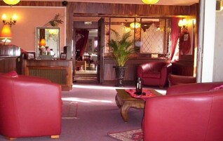 A lobby with red leather sofas, a reception desk, and a potted plant.