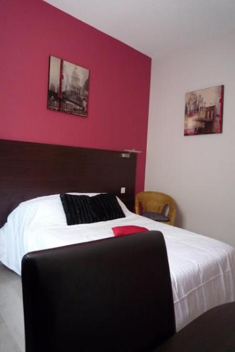 A hotel room with a large bed, a headboard, a chair, and two wall-mounted pictures.