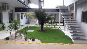 A modern building with a central courtyard featuring a palm tree, surrounded by a well-maintained lawn and various plants. - Hotel Mandino (Alta Floresta)