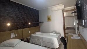 A hotel room with two single beds, a wooden desk, a chair, a television, and an air conditioning unit. - Hotel Mandino (Alta Floresta)