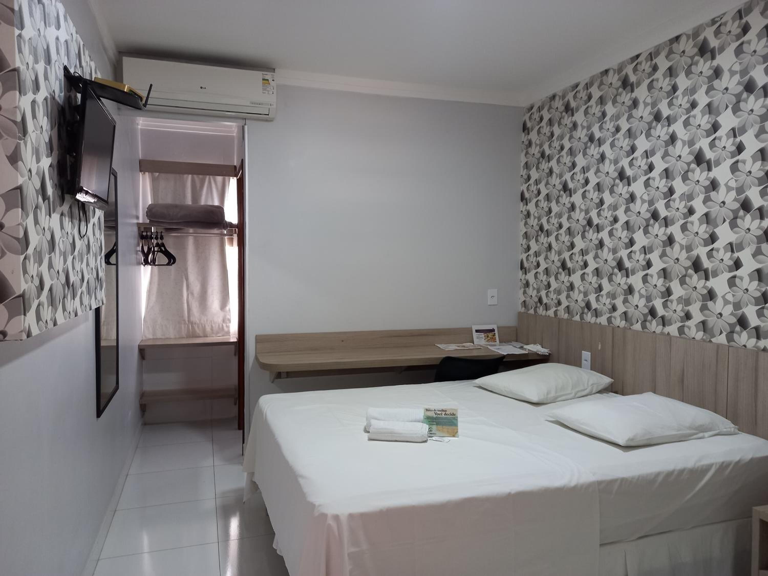 A hotel room with a bed, a desk, a mirror, and a wardrobe.