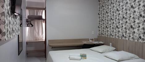 A hotel room with a bed, a desk, a mirror, and a wardrobe.
