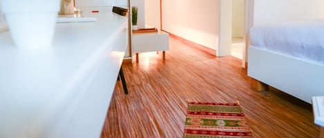 A modern bedroom with a wooden floor, a bed, a nightstand, and a desk with a vase of flowers.