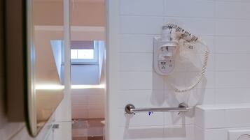 Un baño moderno con una bañera blanca, cabina de ducha con paredes de vidrio, barra para toallas y teléfono instalado en la pared.