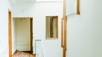 Un hall d’entrée spacieux, doté d’un plancher en bois, d’une lucarne et offrant une vue sur une pièce où se trouve un lit.