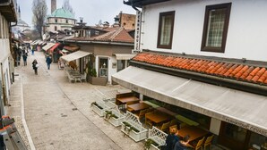 A street with outdoor seating, a building with a sign reading "FERHATOVIC ÇEVAP", and a dome in the background. - Hotel Old Sarajevo (Sarajevo)