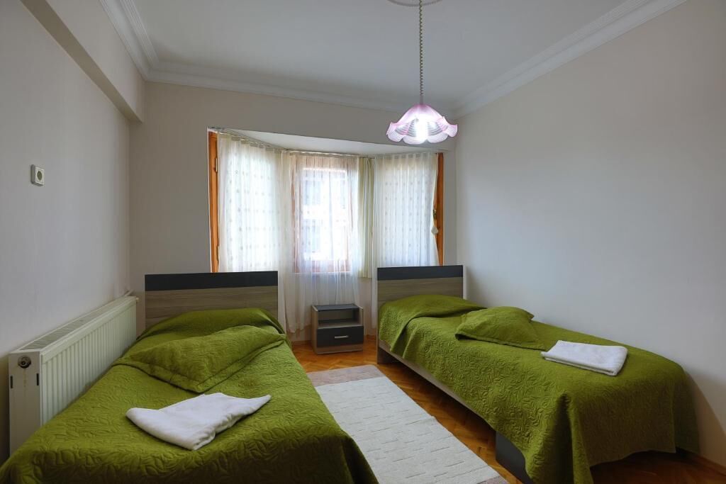 Una habitación con dos camas individuales, un radiador blanco, un tapete blanco y una lámpara colgante.