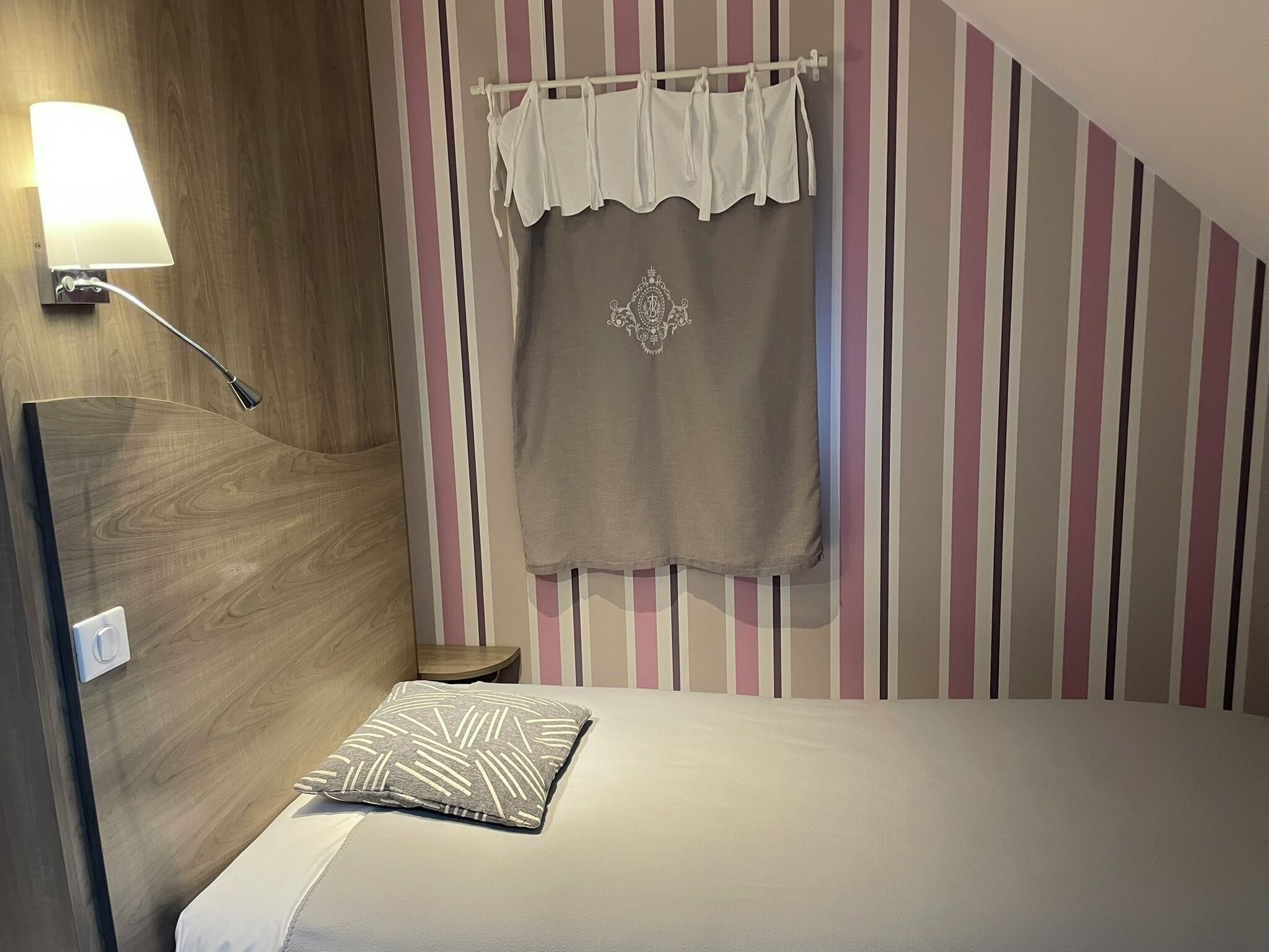 A bedroom with a bed, a nightstand, a lamp, and a striped wall.