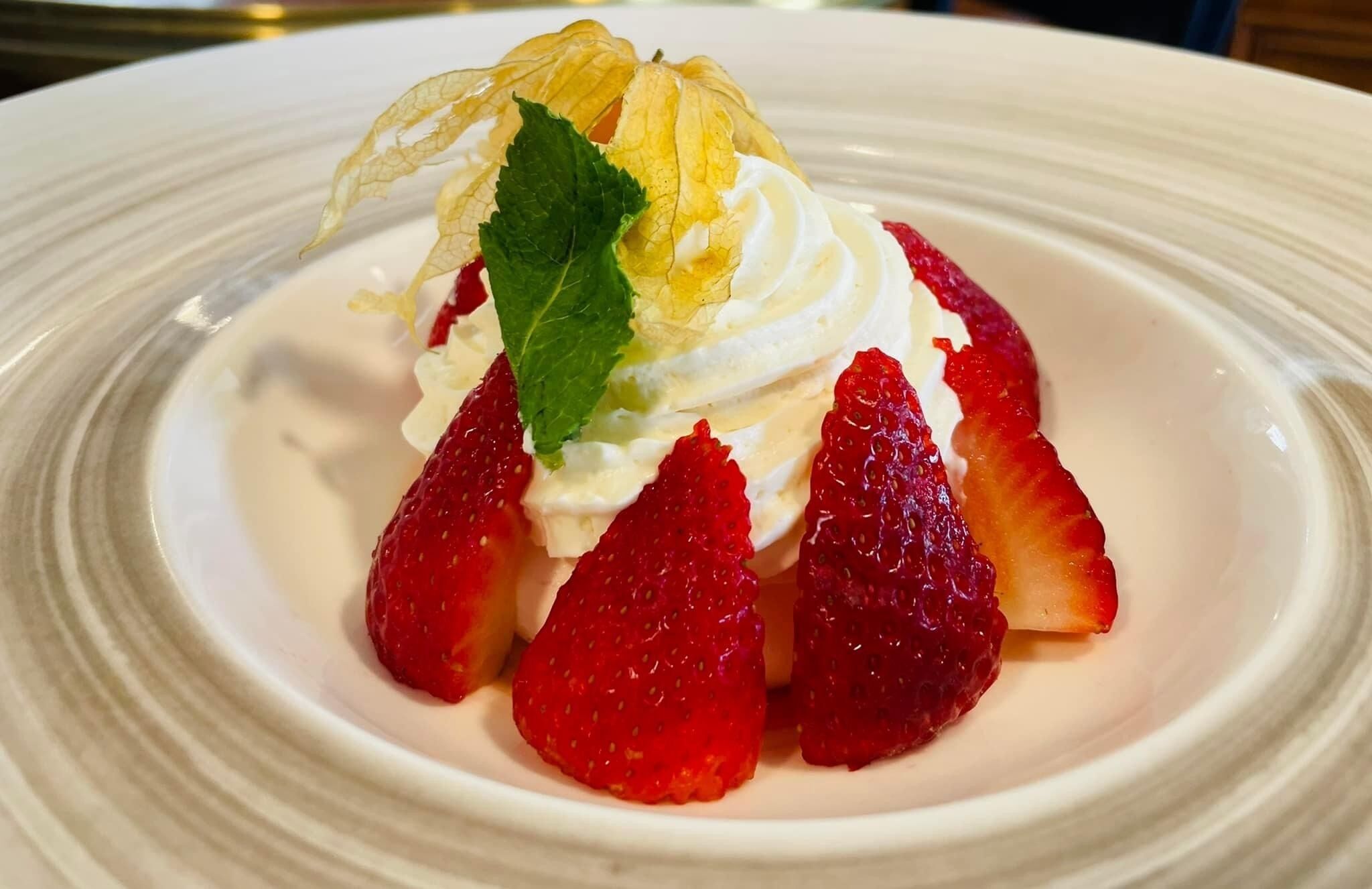 A dessert with strawberries and a leaf garnish on a white plate.