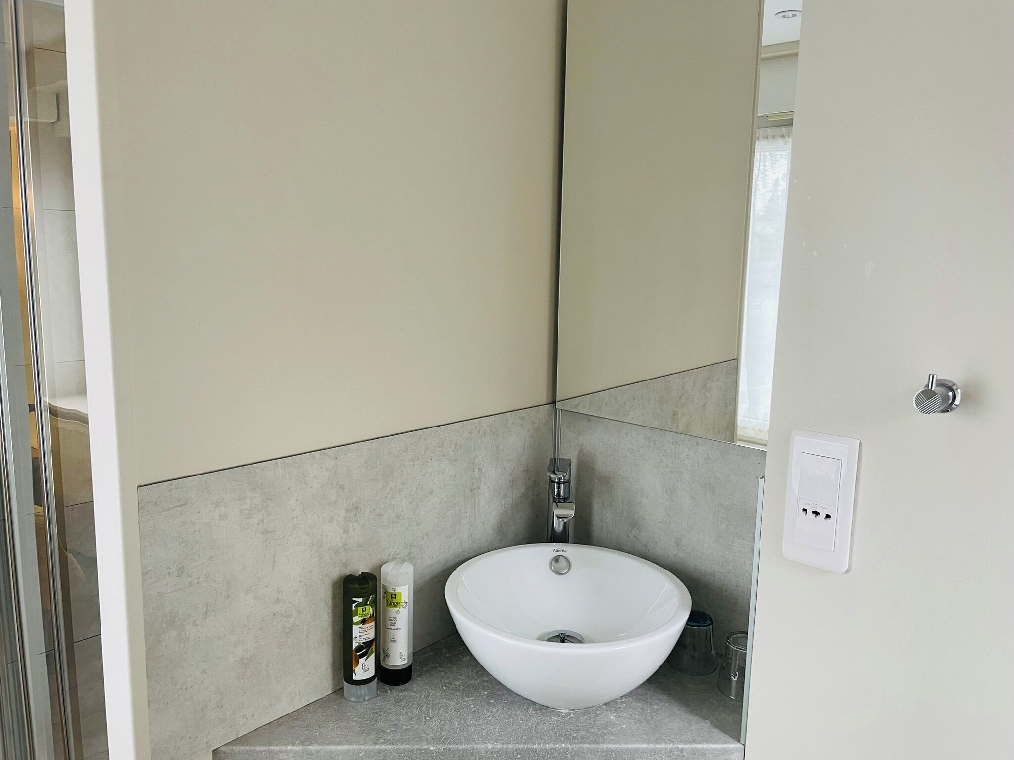 A bathroom with a white sink, a mirror, and a toilet. There are two bottles of hand soap on the counter.