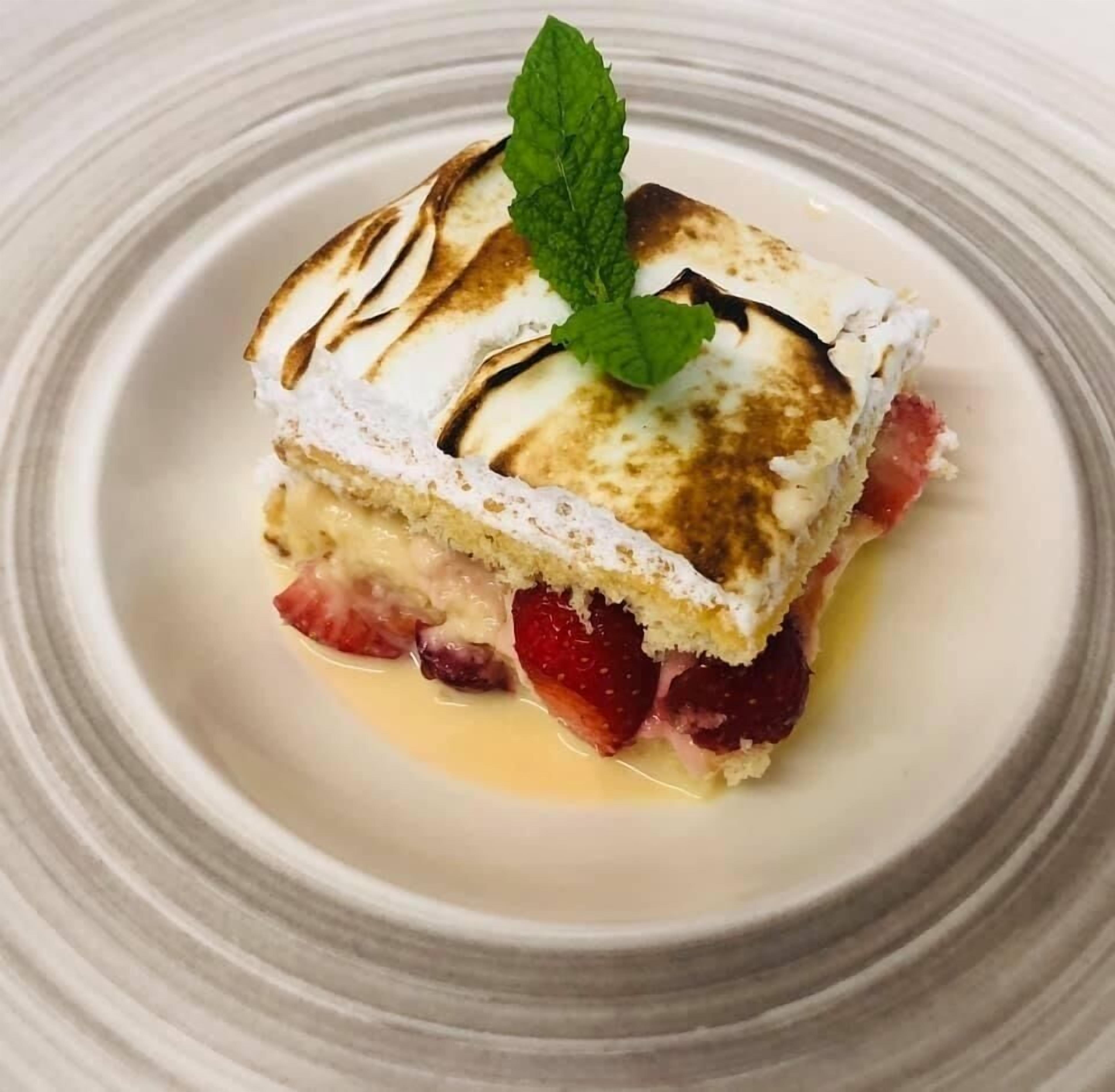 En dessert med marängtopping, jordgubbar och ett myntablad, serverad på en tallrik.