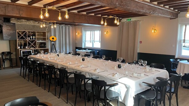 Un restaurante con una larga mesa dispuesta para comer, vigas de madera en el techo y una estantería de vinos al fondo.