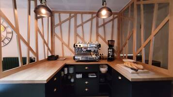 A kitchen area with a coffee machine, two pendant lights, and a clock on the wall.