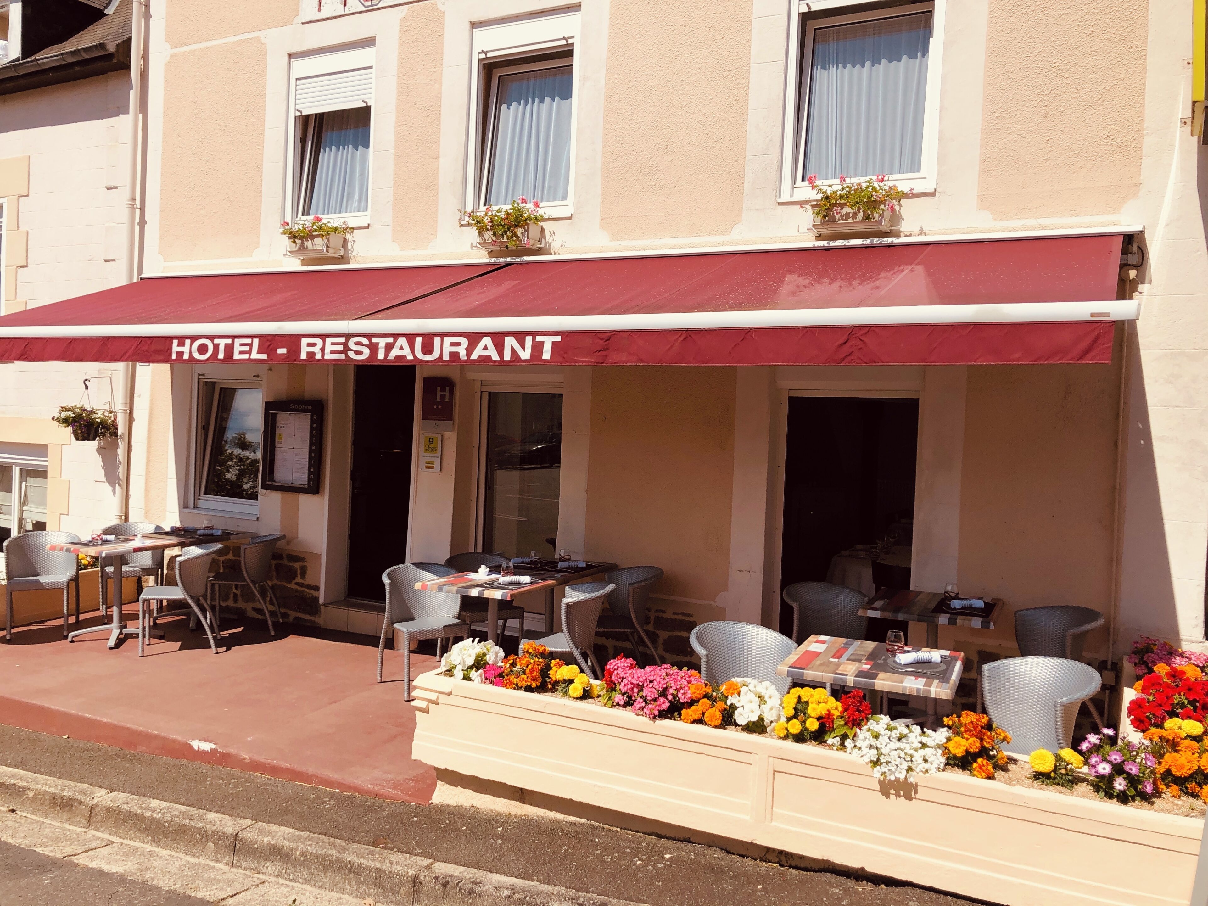 A hotel restaurant with outdoor seating, a red awning, and flower planters.
