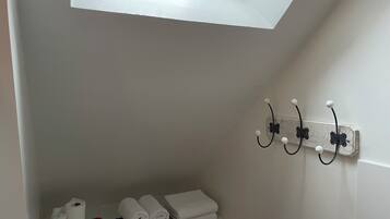 A bathroom with a skylight, a towel rack, and a shelf with towels and toiletries.