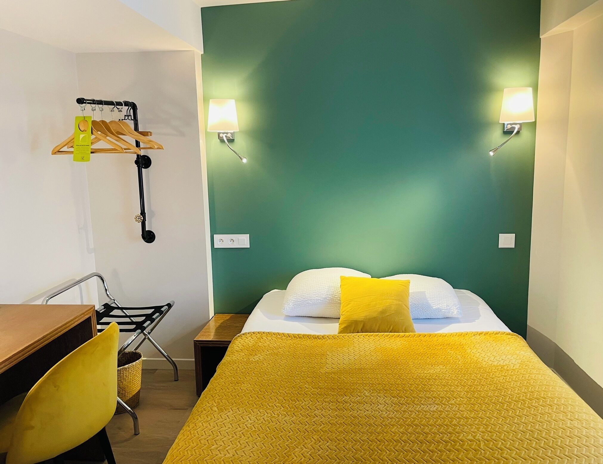 A hotel room with a bed, a desk, a chair, and a wall-mounted coat rack.