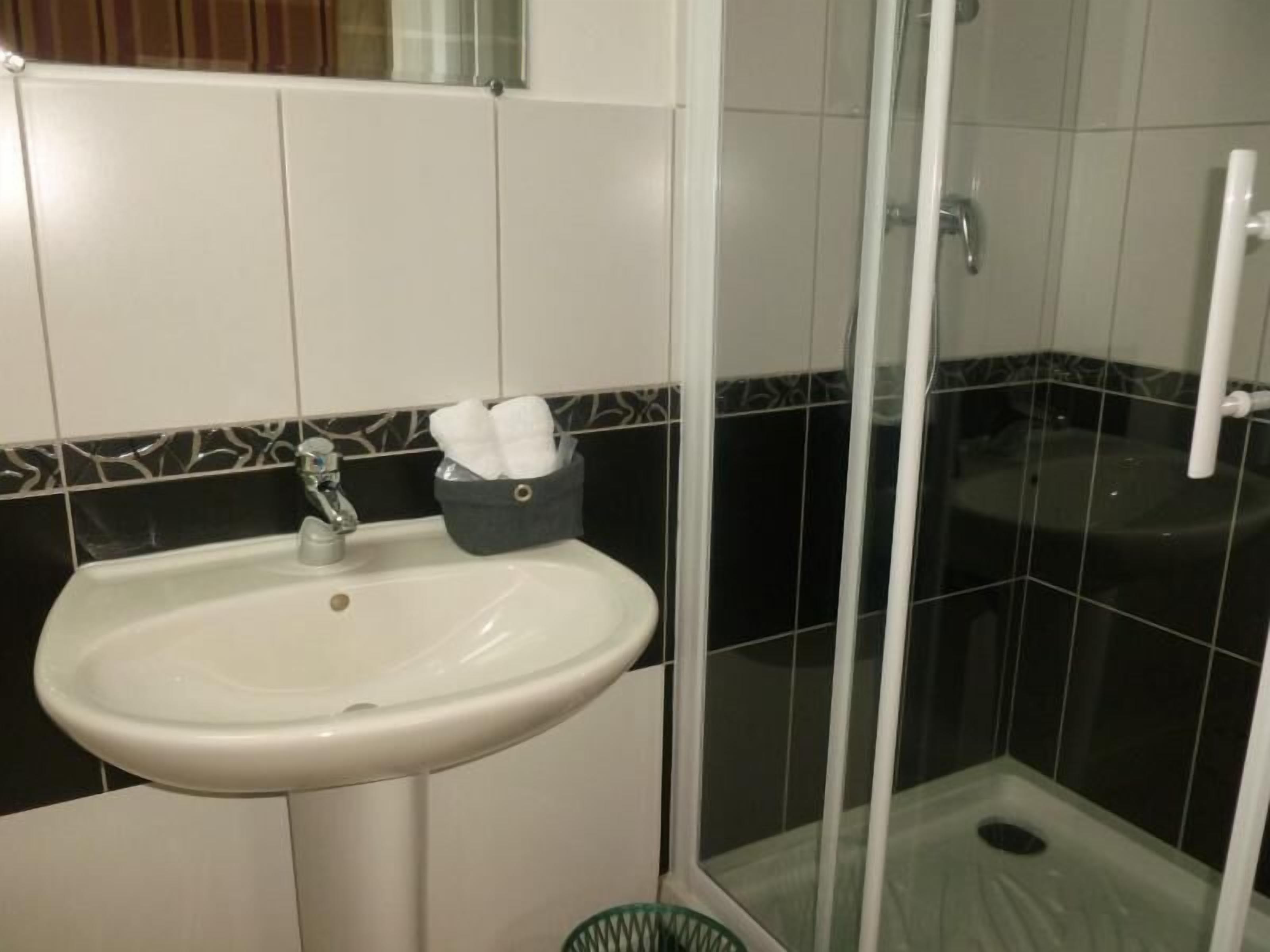 A bathroom with a white sink, a glass shower enclosure, and a black and white tiled wall.