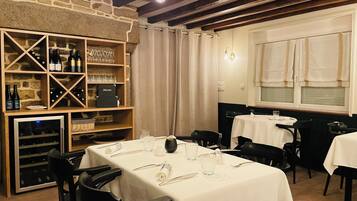 Un restaurante con estantes de madera exhibiendo botellas y copas de vino, mesas dispuestas para comer y una pared de piedra.