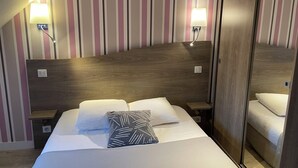 Habitación de hotel con cabecera de madera, dos lámparas de noche, cama con ropa blanca y almohadas estampadas, y piso de madera.