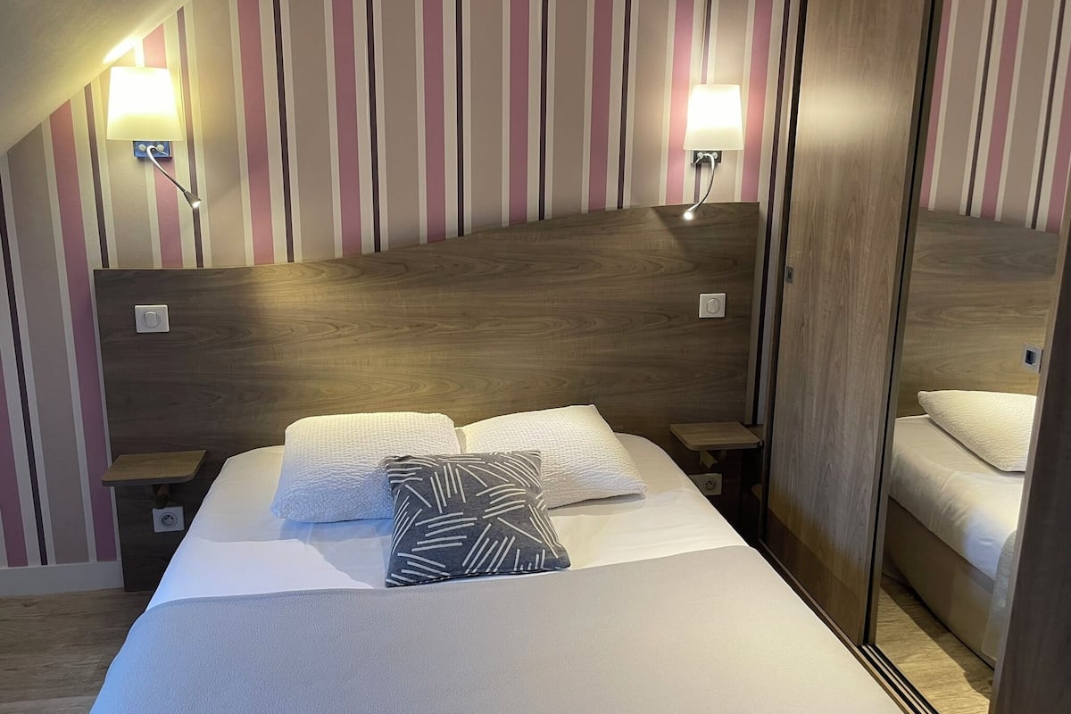 A hotel room with a wooden headboard, two bedside lamps, a bed with white linens and patterned pillows, and a wooden floor.