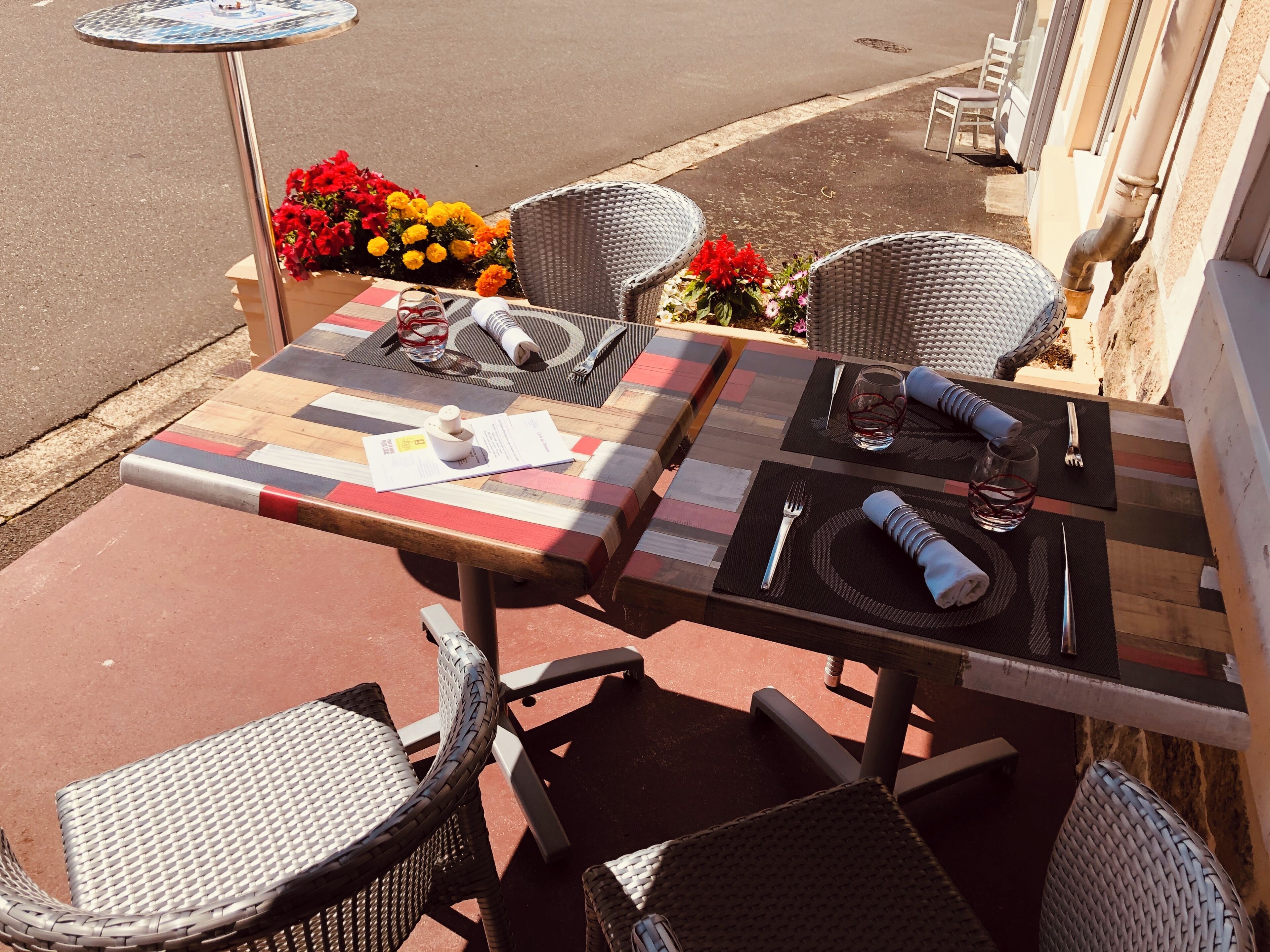 An outdoor dining area with wicker chairs, a wooden table with a striped tablecloth, and a flower arrangement.