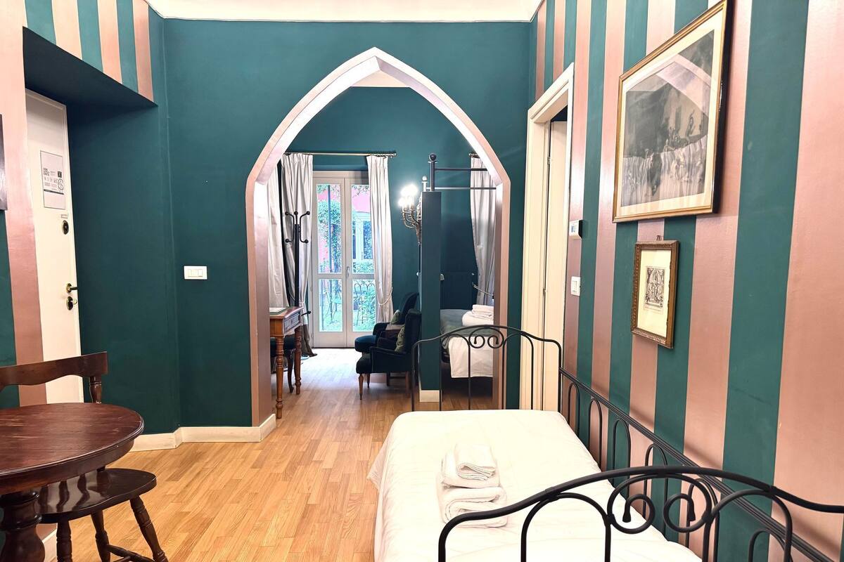 Una habitación con una cama, una mesa y una silla. Hay una puerta que da a otra habitación.