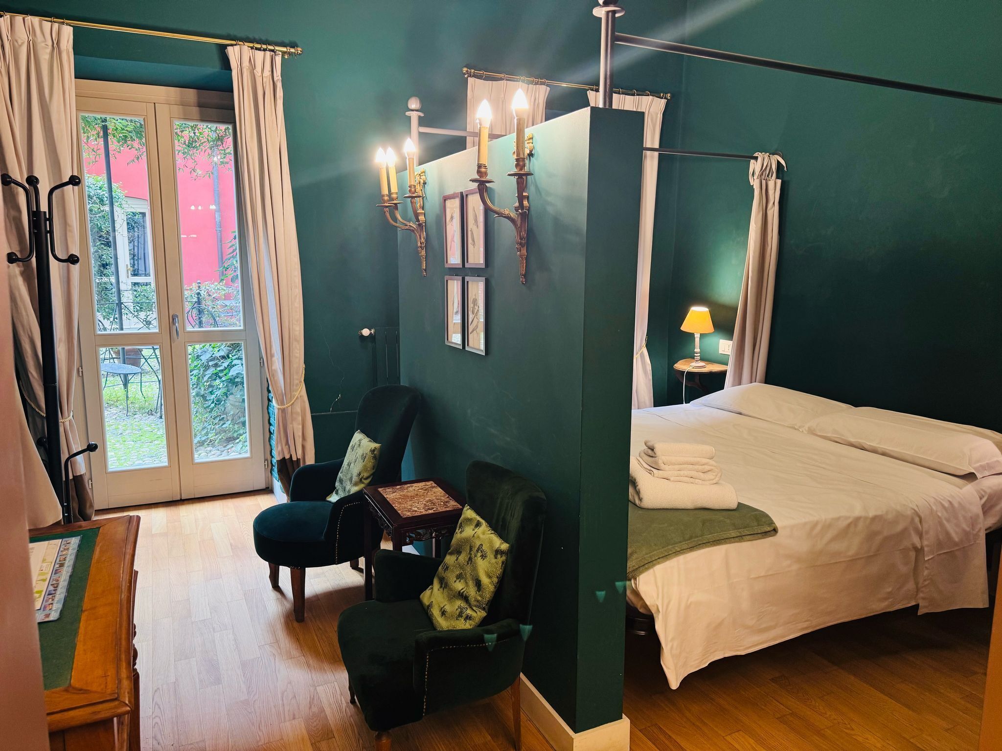 A room with a bed, a chair, a table with a board game, and a window with curtains.