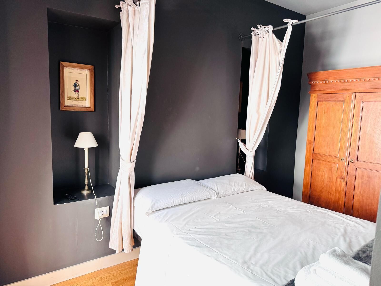 Um quarto com uma cama, mesa de cabeceira, abajur, guarda-roupa e um quadro na parede.