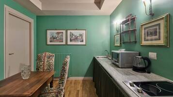 A compact kitchen with a dining area, featuring a wooden table, floral chairs, a built-in oven, and framed pictures on the walls.