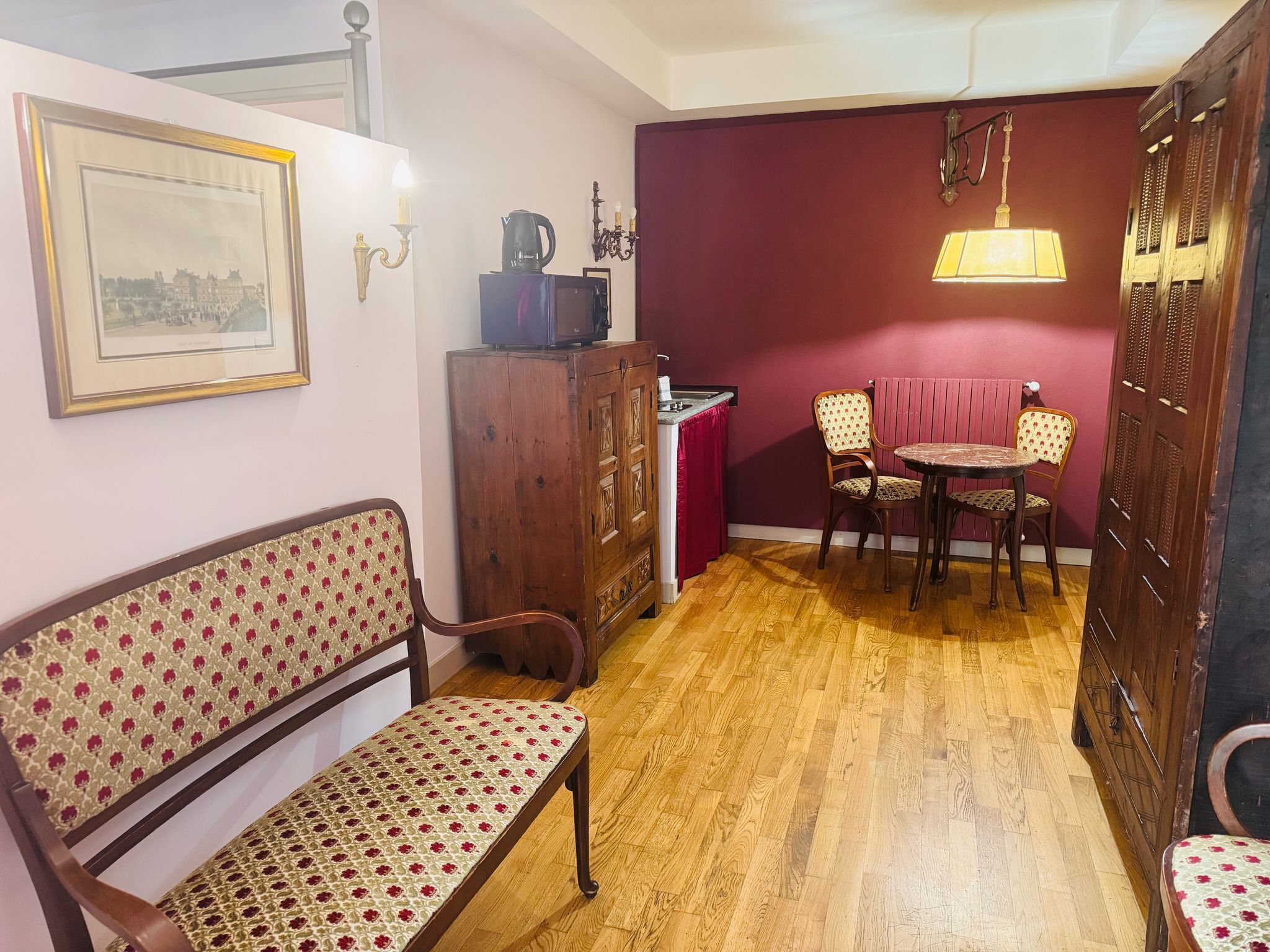 Un espacio habitable compacto con un banco de madera, una pequeña mesa de comedor con dos sillas, un armario con una tetera y un cuadro en la pared.