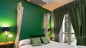A bedroom with a green wall, a bed with white bedding, two green patterned pillows, a window with green curtains, and two bedside lamps. - Residence Porta Palace - Welkome Apartments (Turin)
